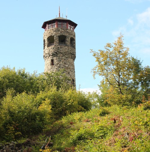 A stone observation tower surrounded by lush greenery and trees under a clear blue sky.