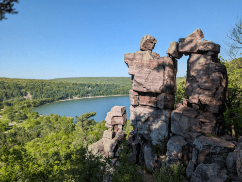 Rock formations overlook a serene lake surrounded by lush greenery under a clear blue sky.