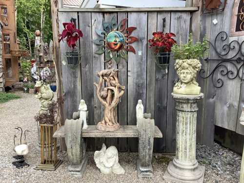 A garden display featuring sculptures, planters, and a decorative sun on a wooden wall.