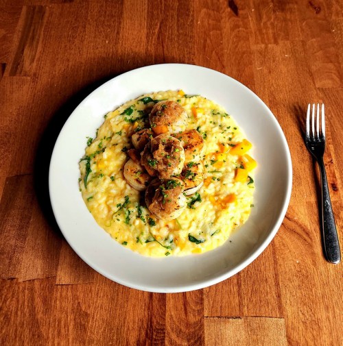 A creamy risotto topped with sautéed shrimp and garnished with herbs, served on a white plate on a wooden table.