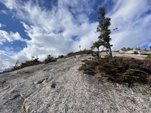 A rocky slope with sparse vegetation under a partly cloudy sky, showcasing a rugged natural landscape.