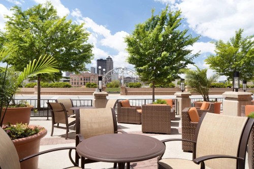 A sunny outdoor patio with seating, greenery, and a view of a city skyline in the background.