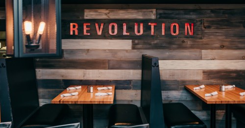 Interior of a restaurant featuring wooden walls and the word "REVOLUTION" in bold red letters above empty tables.