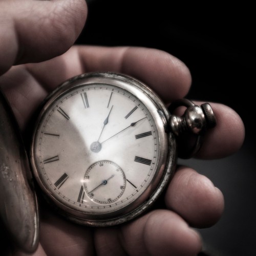 A close-up of a hand holding a vintage silver pocket watch with Roman numerals and a small subdial.