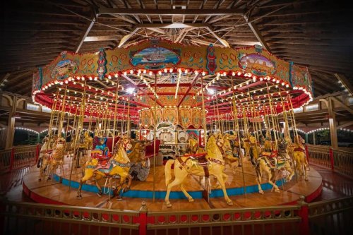A beautifully decorated carousel with golden horses, colorful lights, and intricate designs under a wooden ceiling.