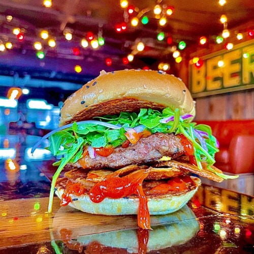 A close-up of a delicious burger with lettuce, sauce, and a sesame seed bun, set against a colorful, festive background.