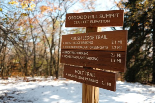Wooden signpost at Osgood Hill Summit, listing trails and distances: Kulish Ledge Trail and Holt Trail. Snow on the ground.
