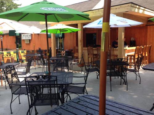 Outdoor seating area with black metal tables and chairs, shaded by green umbrellas, in a rustic wooden setting.