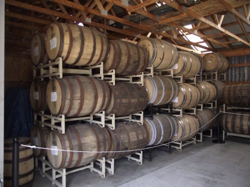 A stack of wooden barrels stored on racks inside a rustic barn.