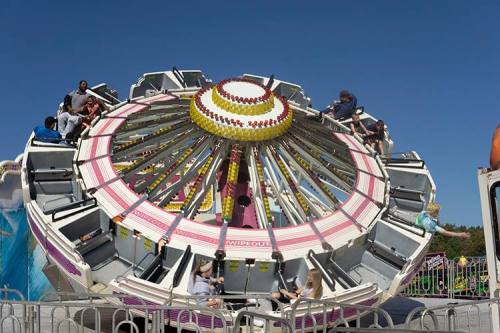 A colorful amusement park ride spins with excited riders enjoying the thrill under a clear blue sky.