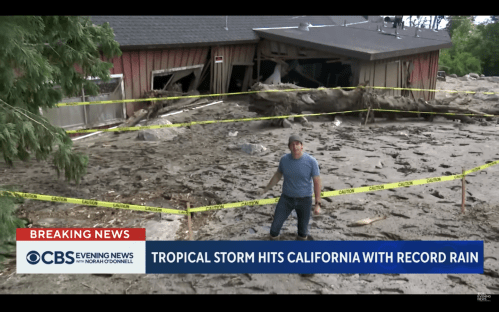 A reporter stands near a damaged building surrounded by caution tape after a tropical storm in California.