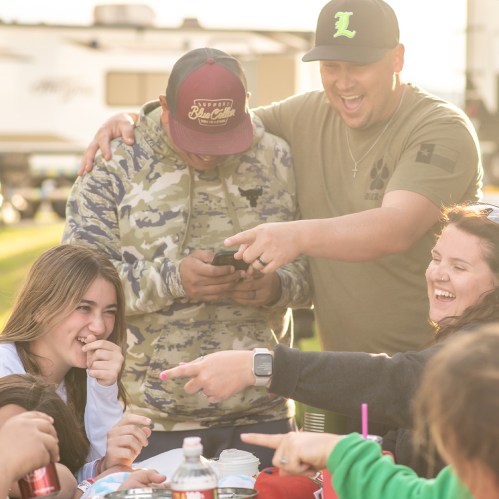 A group of friends laughing and enjoying a meal together outdoors, sharing joyful moments and playful interactions.