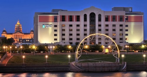 A hotel building at dusk, with a lit ferris wheel and city skyline in the background along a riverbank.