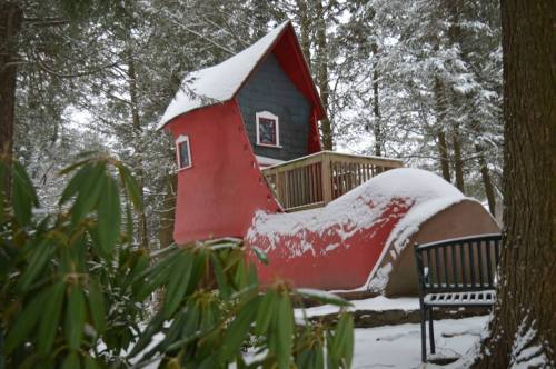 A whimsical red shoe-shaped house nestled in a snowy forest, surrounded by evergreen trees.