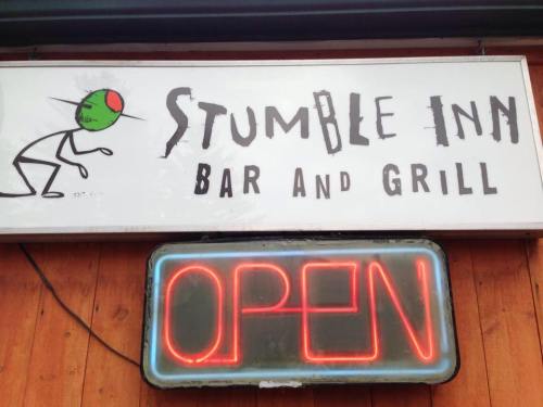 Sign for "Stumble Inn Bar and Grill" with a green olive character and a glowing "OPEN" neon sign below.