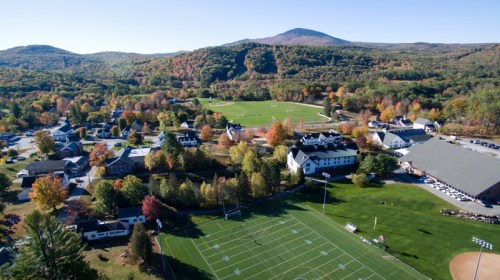 Aerial view of a scenic campus surrounded by autumn foliage and mountains, featuring sports fields and buildings.