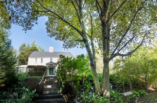 A charming house with a front staircase, surrounded by lush greenery and a tree with a swing in the yard.