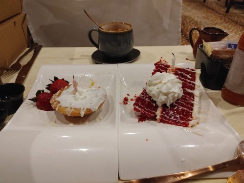 A plate with a cupcake and red velvet cake, both topped with whipped cream, alongside a cup of coffee.