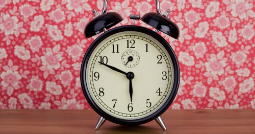 A vintage black alarm clock on a wooden surface, with a floral patterned background. The time shows 10:10.