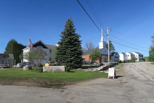 A small town sign for Munsonville, with a church and houses in the background under a clear blue sky.