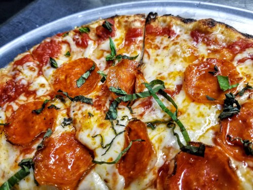 Close-up of a pizza topped with pepperoni, melted cheese, and fresh basil on a metal tray.