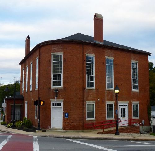 Historic brick building with large windows, two chimneys, and a red railing, located at a street corner.