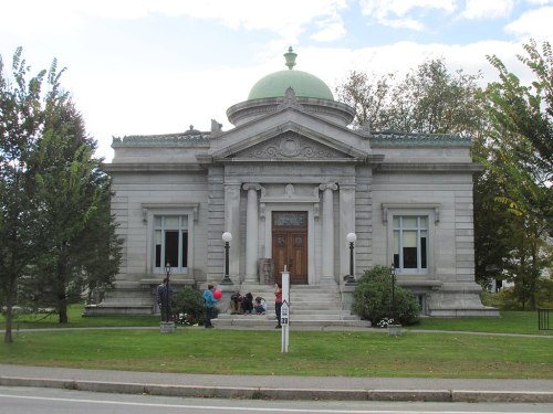 A historic stone building with a green dome, surrounded by trees and people sitting on the steps.