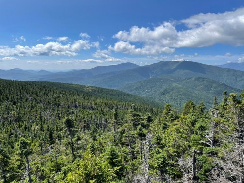 A panoramic view of lush green mountains under a blue sky with scattered clouds.