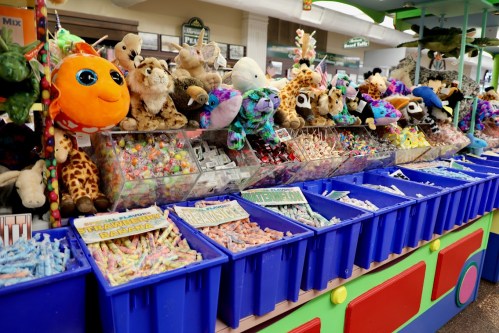 A colorful display of stuffed animals and bins filled with various candies at a fair or carnival.