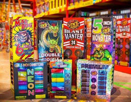 Colorful boxes of fireworks, including canister shells and assorted types, displayed in a store aisle.