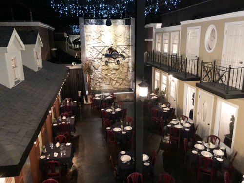 A cozy restaurant interior with tables set for dining, surrounded by charming decor and a stone wall feature.