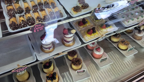 A display case filled with various colorful mini desserts, including cakes, cannoli, and fruit-topped treats.