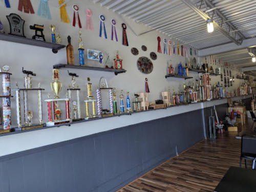 A wall displaying various trophies, awards, and ribbons in a well-organized room with wooden flooring.