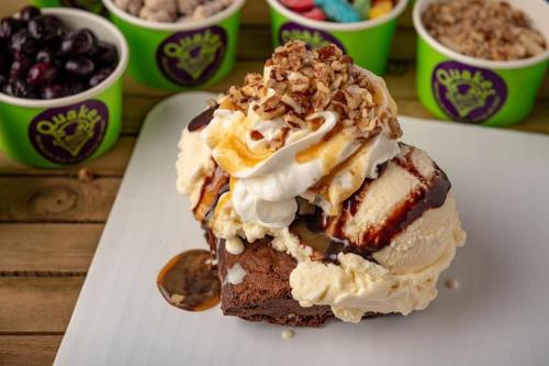 A decadent dessert featuring a brownie topped with vanilla ice cream, whipped cream, nuts, and chocolate sauce.