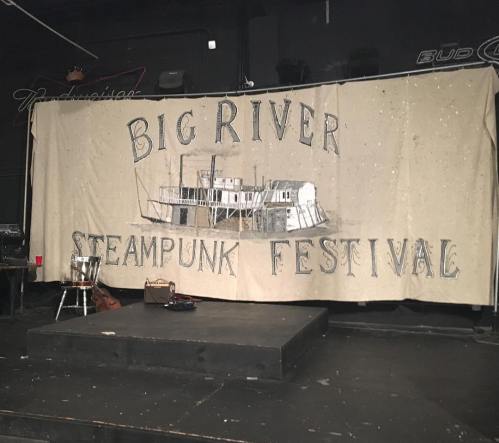 A stage backdrop for the "Big River Steampunk Festival" featuring a steamboat illustration.