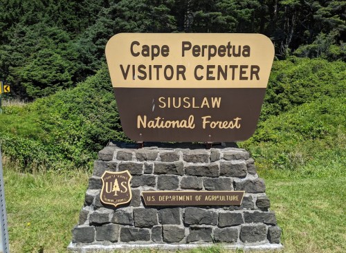 Sign for Cape Perpetua Visitor Center, Siuslaw National Forest, with a stone base and U.S. Department of Agriculture emblem.