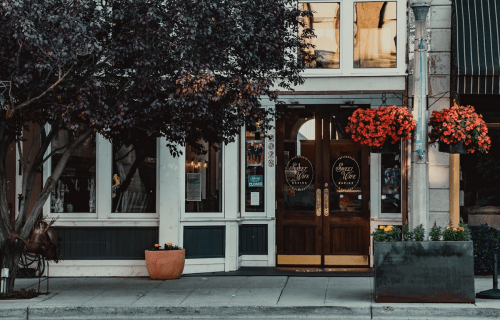 A charming restaurant entrance with wooden doors, vibrant flower baskets, and a tree in front.