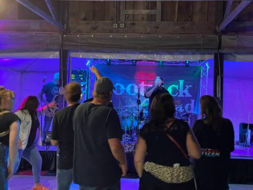 A lively band performs on stage while an audience dances in a colorful, illuminated venue.