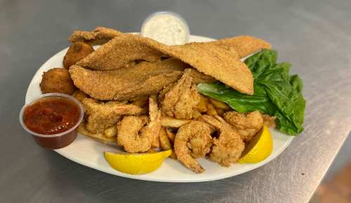 A plate of fried fish, shrimp, fries, and lettuce, served with dipping sauces and lemon wedges.