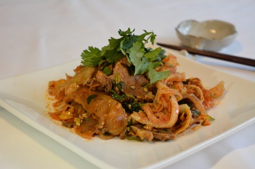 A plate of spicy beef salad topped with fresh cilantro, served on a white dish with chopsticks in the background.