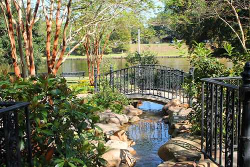 A serene garden scene featuring a small bridge over a stream, surrounded by lush greenery and trees.