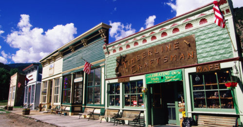 Colorful historic buildings line a street, featuring shops with signs and American flags under a blue sky with clouds.