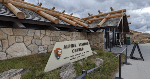 Exterior of the Alpine Visitor Center, featuring stone walls and wooden beams, with a sign displaying its name.