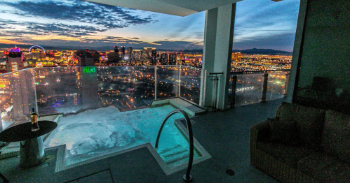 A luxurious balcony with a hot tub overlooking a vibrant city skyline at sunset.