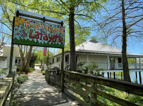 Colorful sign reading "Bienvenue à Lafayette" near a wooden walkway leading to a building by the water.