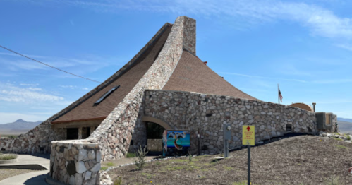 A unique stone building with a sloped roof, set against a clear blue sky and surrounded by arid landscape.
