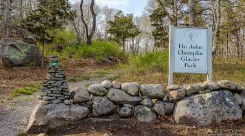 Sign for Dr. John Champlin Glacier Park, surrounded by stone walls and greenery, with a path leading into the park.