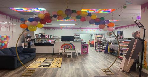 A colorful party space with a balloon arch, candy-themed decor, and a cozy seating area.