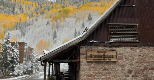 A rustic building with a wooden sign, surrounded by snow-covered trees and vibrant autumn foliage in the background.