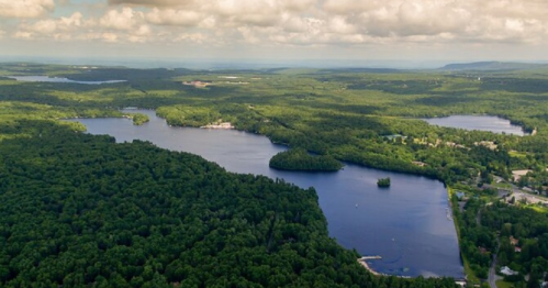 Aerial view of lush green forests surrounding a serene lake under a partly cloudy sky.